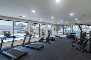 Une salle de sport équipée de tapis de course, d’un appareil elliptique et de machines de musculation, avec de grandes fenêtres donnant sur l’extérieur.