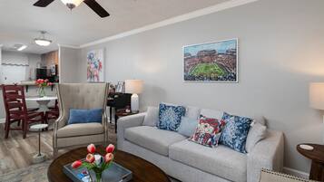 A living room with a sofa, a coffee table with tulips, a dining area with a piano, and a ceiling fan.