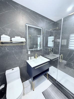 Une salle de bain moderne avec une douche à parois de verre, un lavabo blanc doté de robinets dorés et des toilettes.