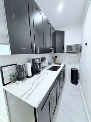 Une cuisine moderne avec des meubles de couleur sombre, un plan de travail blanc et un four à micro-ondes.
