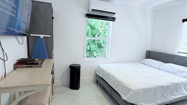 Una stanza con un letto, una scrivania, una sedia, una ventola a soffitto, un condizionatore d'aria e una finestra vista verde.