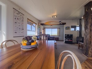 A spacious living area with a wooden dining table, a large window, and a surfboard decoration.