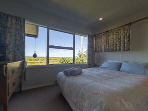 A bedroom with a large window, a bed with a floral bedspread, a wooden dresser, and a hanging light fixture.
