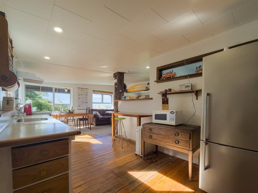 A kitchen with wooden flooring, a refrigerator, a microwave, and a wooden cabinet.