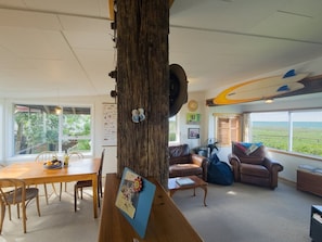 A living room with a wooden tree trunk centerpiece, a dining area with a table and chairs, a brown leather sofa, and a surfboard on the wall.