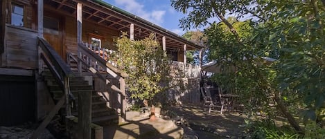 A wooden house with a porch, a stone pathway, and a small garden area.