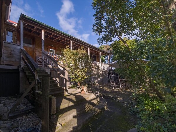 A wooden house with a porch, a stone pathway, and a small garden area.