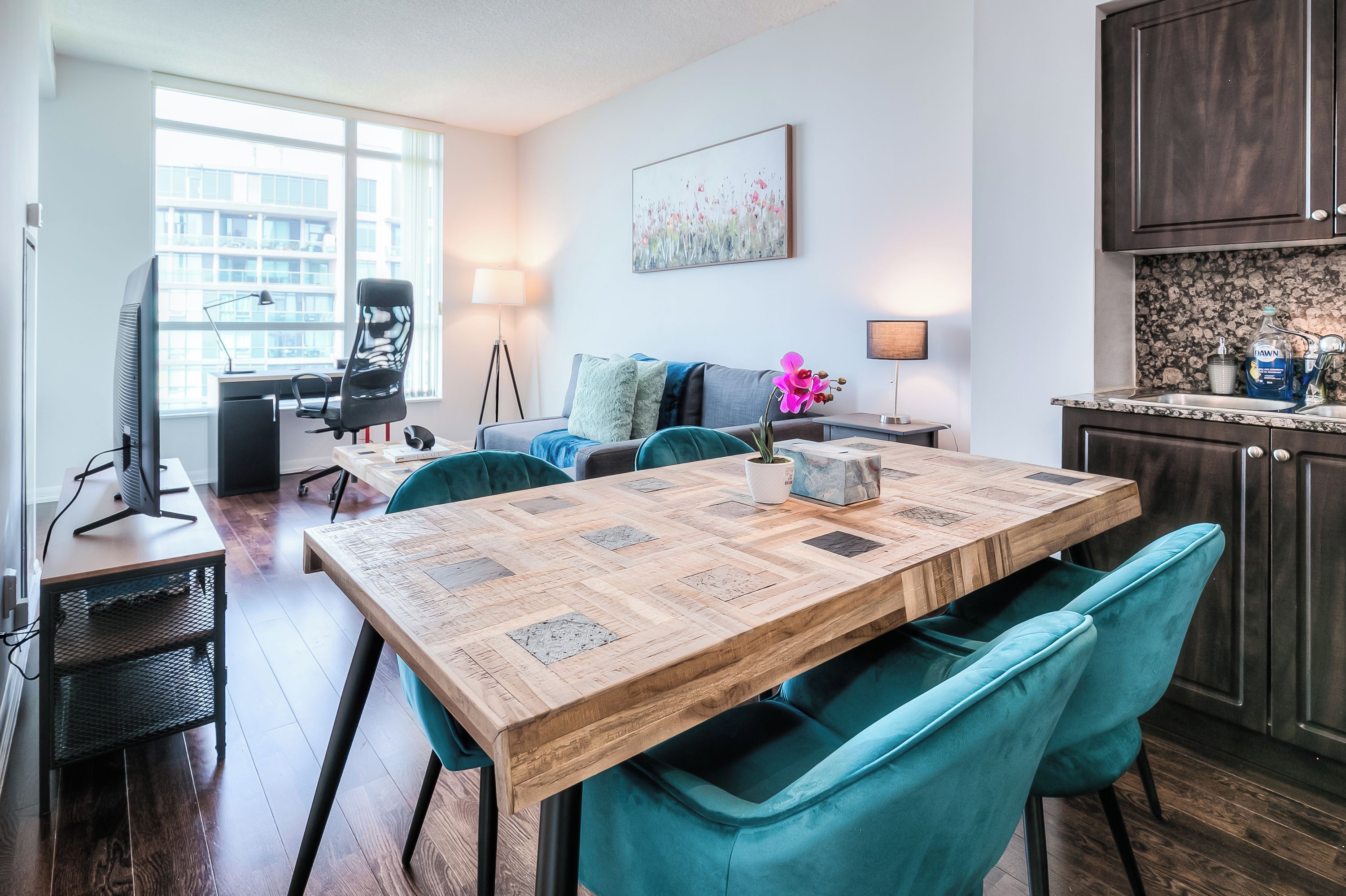 Een moderne woonkamer met een houten eettafel, teal gekleurde stoelen, een bank en een televisie.