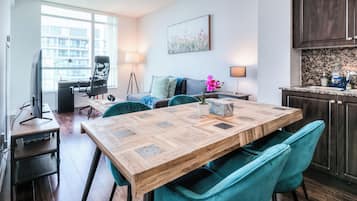 Een moderne woonkamer met een houten eettafel, teal gekleurde stoelen, een bank en een televisie.