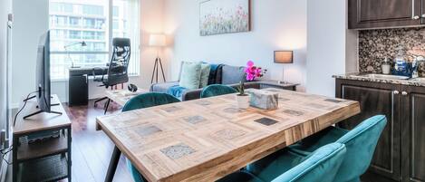 A modern living room with a wooden dining table, teal chairs, a sofa, and a TV.