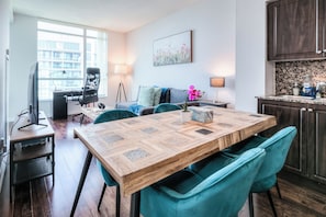 A modern living room with a wooden dining table, teal chairs, a sofa, and a TV. - StayToronto - The Fort York Suites (Toronto)