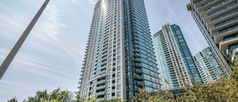 A high-rise building with multiple floors and balconies, surrounded by trees and other buildings.