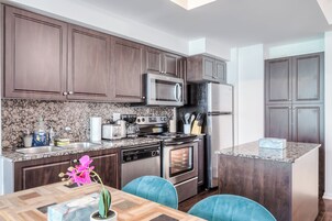 Een moderne keuken met donkerhouten kasten, roestvrijstalen apparatuur, granieten aanrechtbladen en teal-kleurige stoelen.