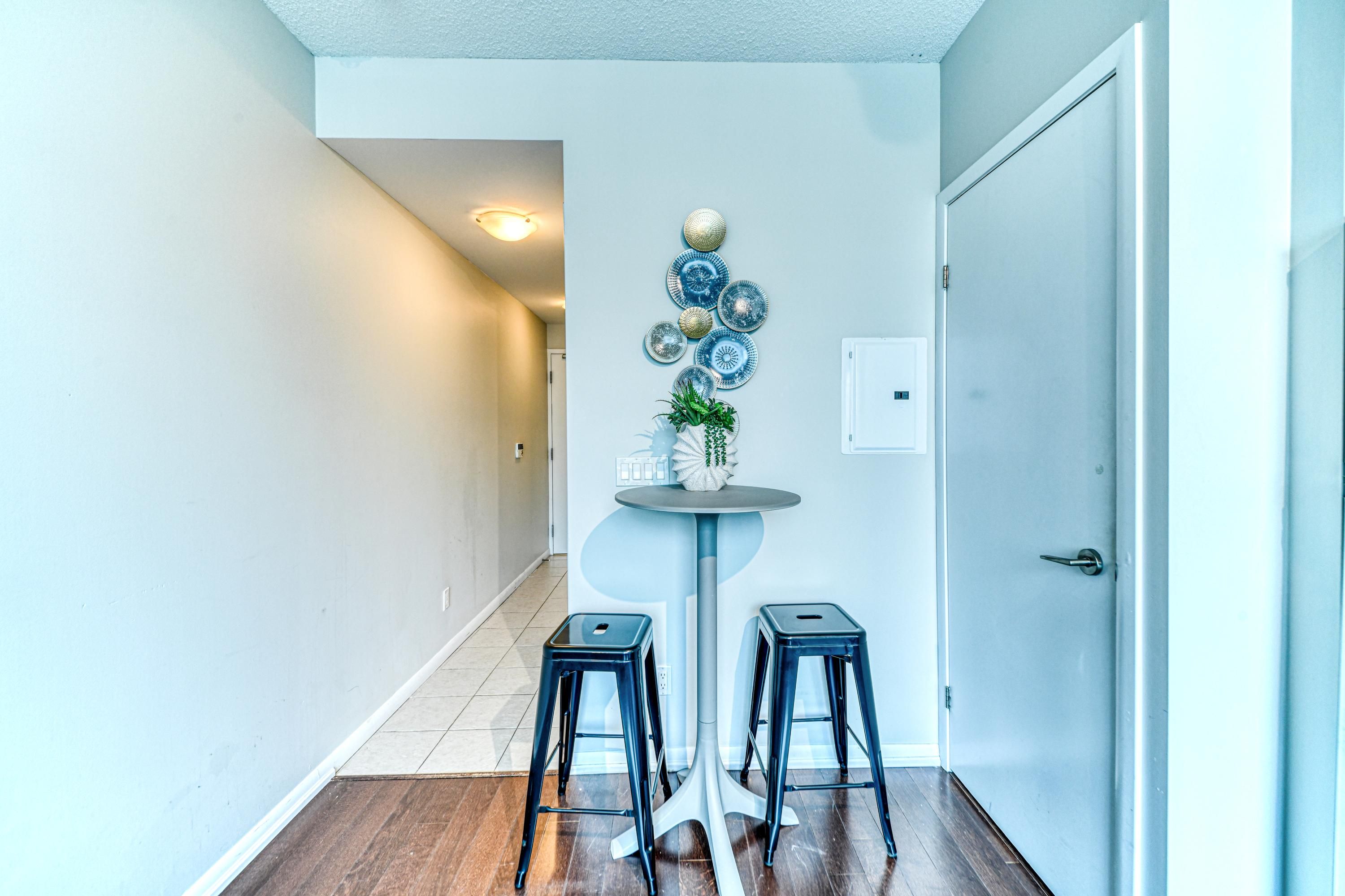 A hallway with a round table, two stools, a wall-mounted plate decoration, and a door.