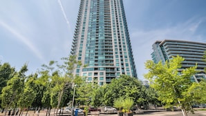 Ein hohes, modernes Hochhaus mit gewölbter Fassade, umgeben von Bäumen und blauem Himmel.