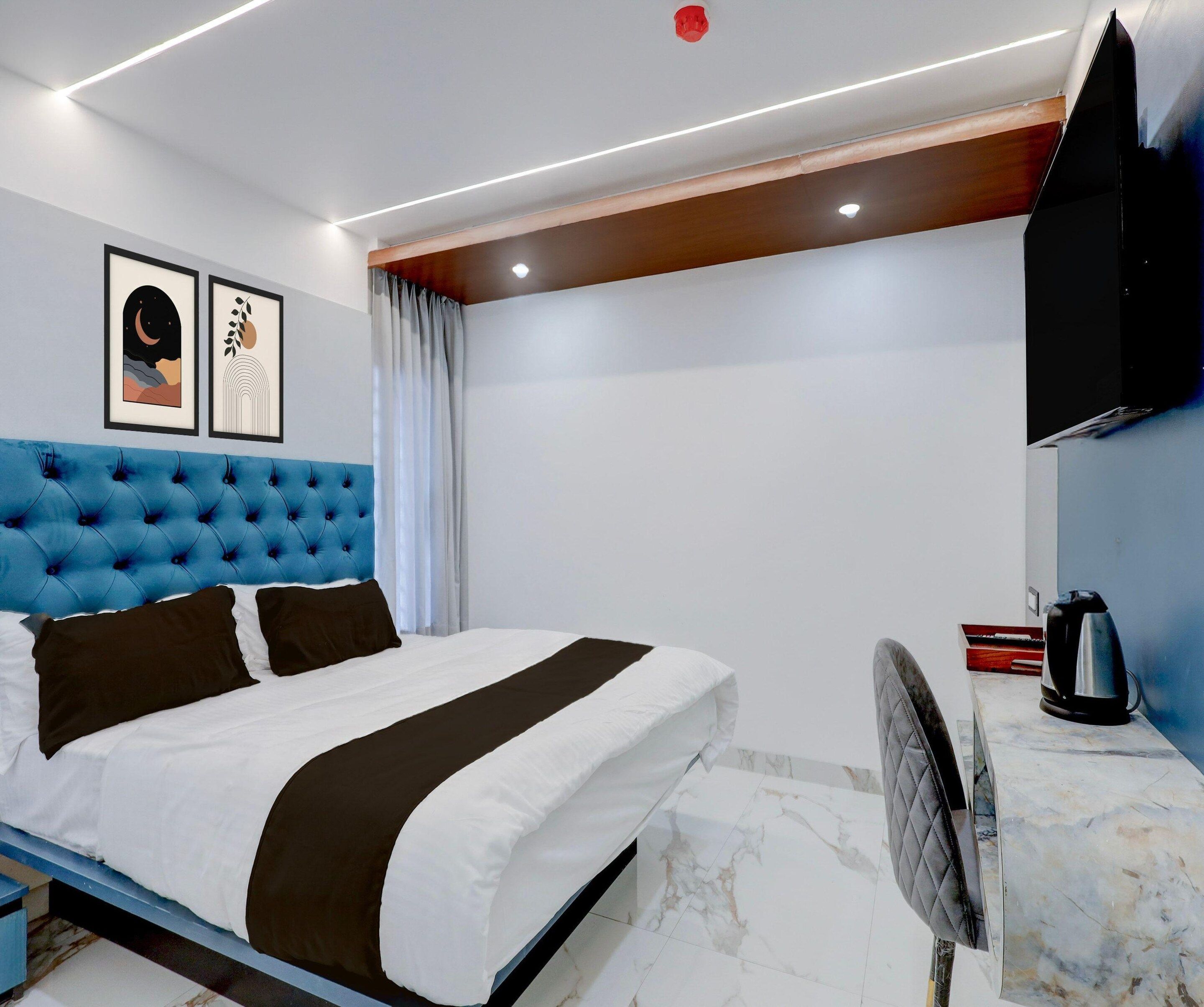 Un dormitorio moderno con un cabecero azul capitonado, una cama con ropa de cama blanca y marrón oscuro, un televisor de pantalla plana montado en la pared y un suelo con estampado de mármol.