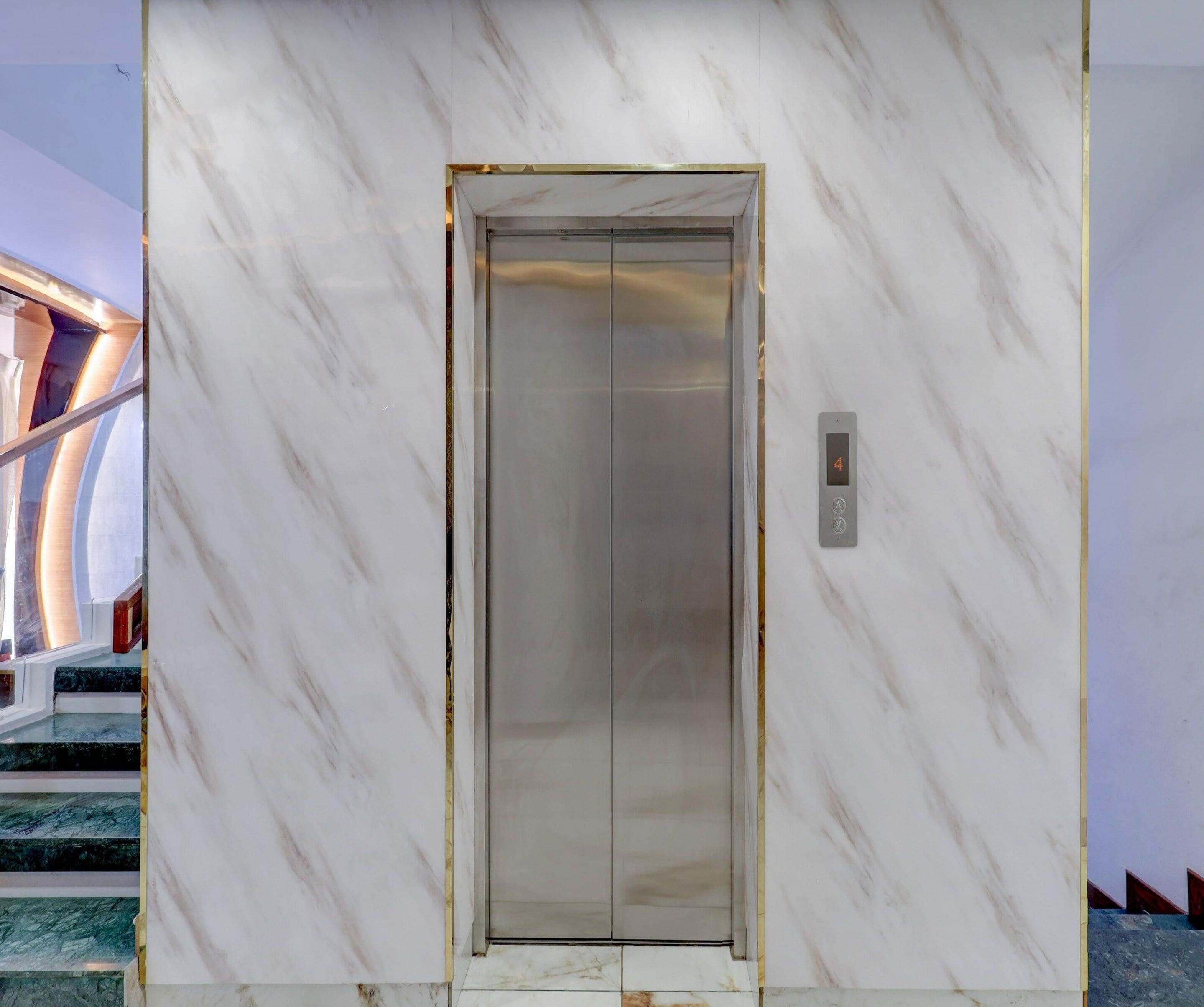 An elevator with a marble wall, a digital display, and a staircase with a glass railing.