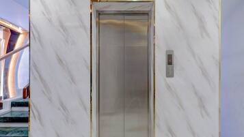 An elevator with a marble wall, a digital display, and a staircase with a glass railing.