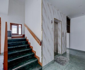 Eine Treppe mit dunklen Stufen und hölzernen Geländern, die zu einem Raum mit einer Marmorwand und einer Tür mit Telefon führt.