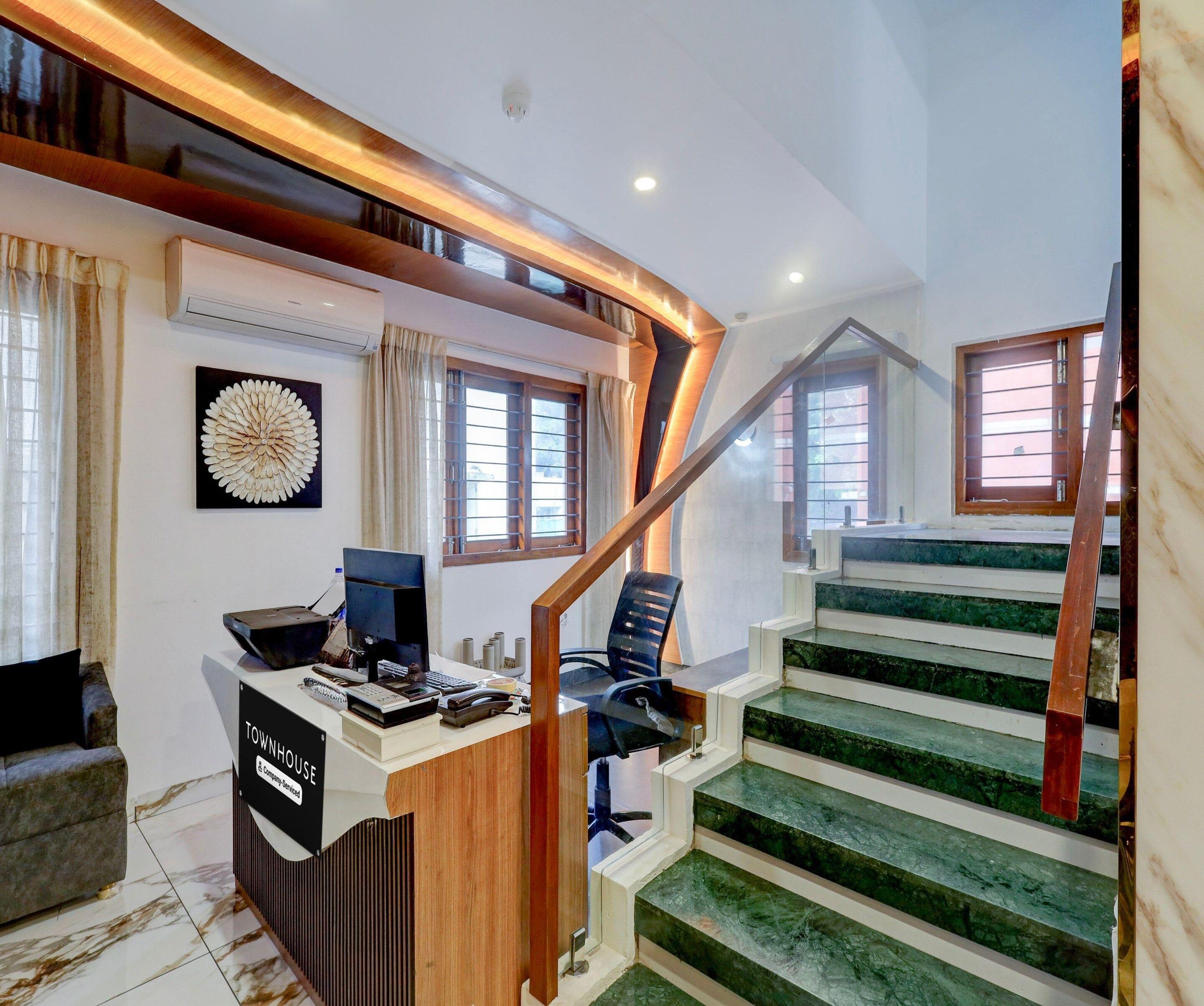 A modern interior with a desk, computer, and chair, a staircase with green steps, and a decorative wall piece.