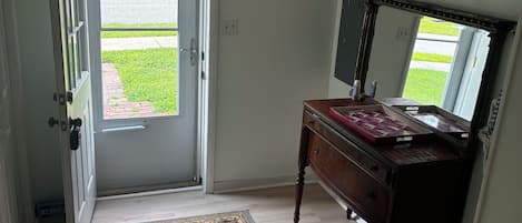 Un pasillo con suelo de madera, un tapete, un banco y una puerta que da al exterior.