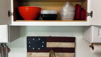 Una cucina con uno scaffale di legno sopra un lavello, su cui sono esposti utensili da cucina e una bandiera americana decorativa.