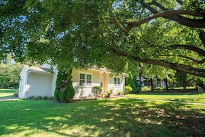 A single-story house with a front porch, surrounded by a well-maintained lawn and trees.