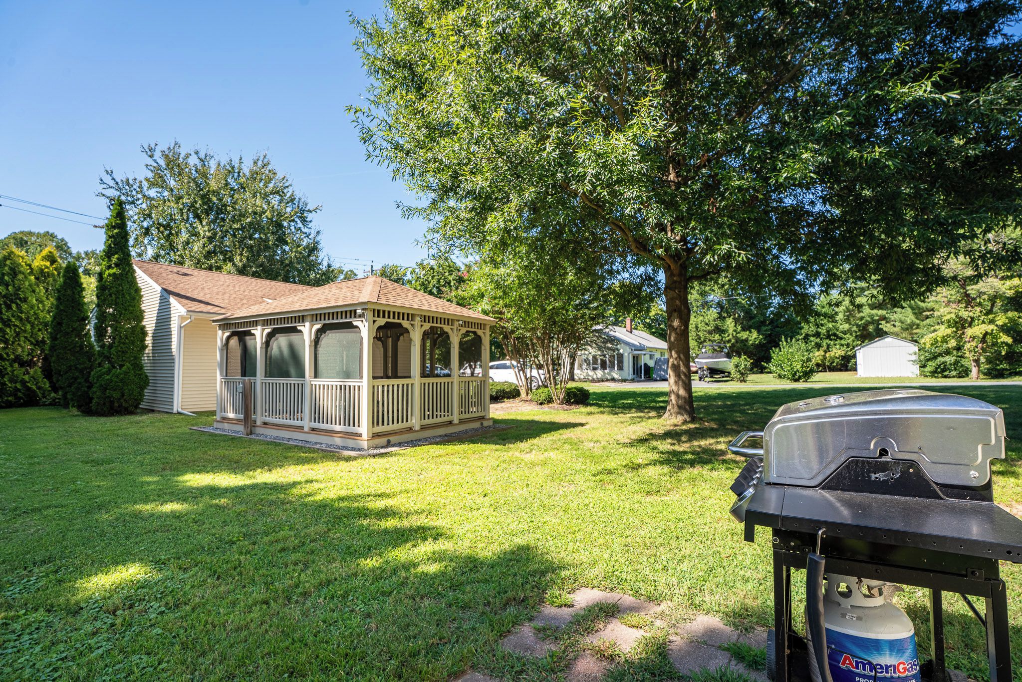 Een huis met een overdekte veranda, een barbecue en een propaantank in de tuin.
