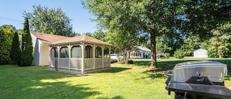 A house with a covered porch, a grill, and a propane tank in the yard.