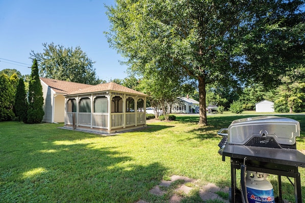 A house with a covered porch, a grill, and a propane tank in the yard.