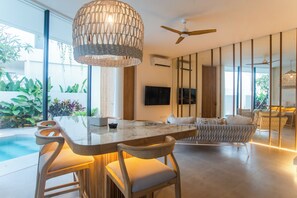 Ein modernes Interieur mit Essbereich, Bar und Deckenventilator, sowie ein großes Fenster mit Blick auf einen Pool.