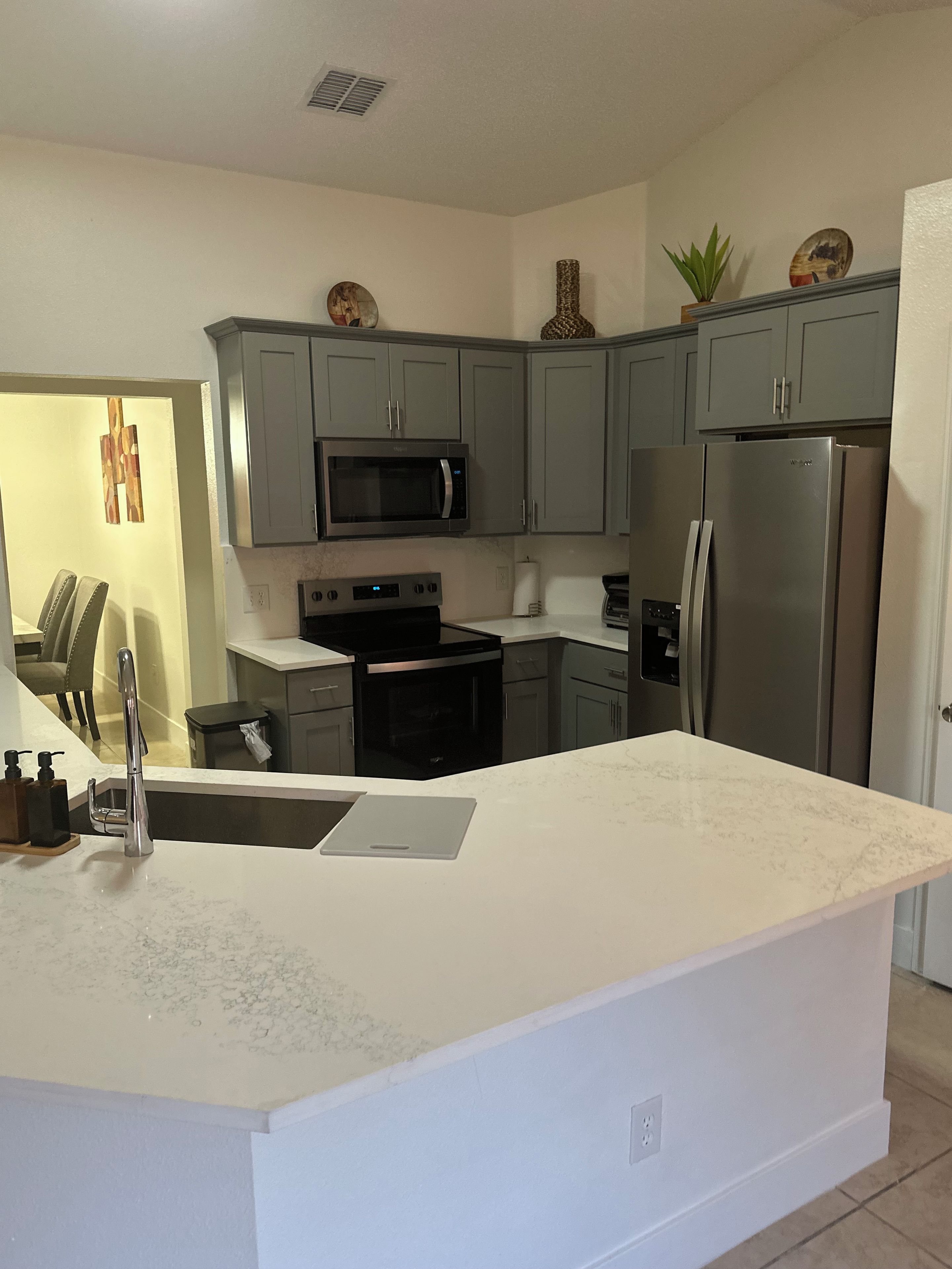 A modern kitchen with grey cabinets, a stainless steel refrigerator, a microwave, and a built-in oven.