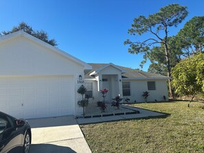 A residential house with a garage, a front porch, and a well-maintained lawn. - Sunny Palm Bay Getaway  3 Bedrooms, 2 Baths & Air Conditioning. (Palm Bay)