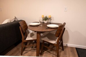 A dining area with a round wooden table, two chairs, and a small plant on the table. - Modern Studio - Full Kitchen (Grandview)