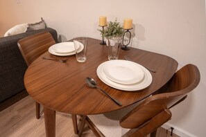 A round wooden dining table with white plates, a glass, and a candle holder with candles. - Modern Studio - Full Kitchen (Grandview)