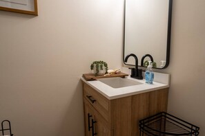 A bathroom with a white sink, wooden cabinet, and a mirror. - Modern Studio - Full Kitchen (Grandview)