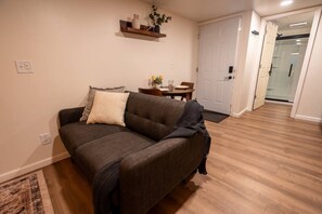 A living room with a sofa, a small table with a vase and candles, and a door leading to another room. - Modern Studio - Full Kitchen (Grandview)