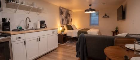 Een knus woongedeelte met een kitchenette, een bed, een eethoek en een groot kunstwerk aan de wand.