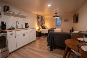 A compact living space with a kitchenette, a bed, a dining area, and a large artwork on the wall. - Modern Studio - Full Kitchen (Grandview)