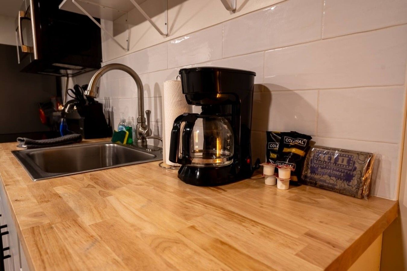 A kitchen with a coffee maker, a sink, and a bag of butter.