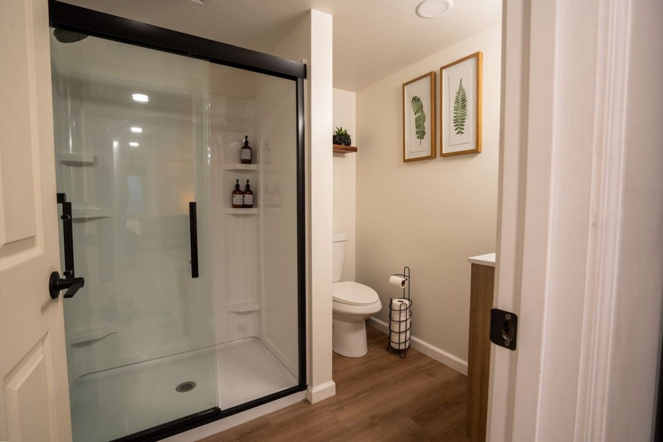 Un bagno moderno con box doccia in vetro, un WC e stampe botaniche incorniciate alle pareti.