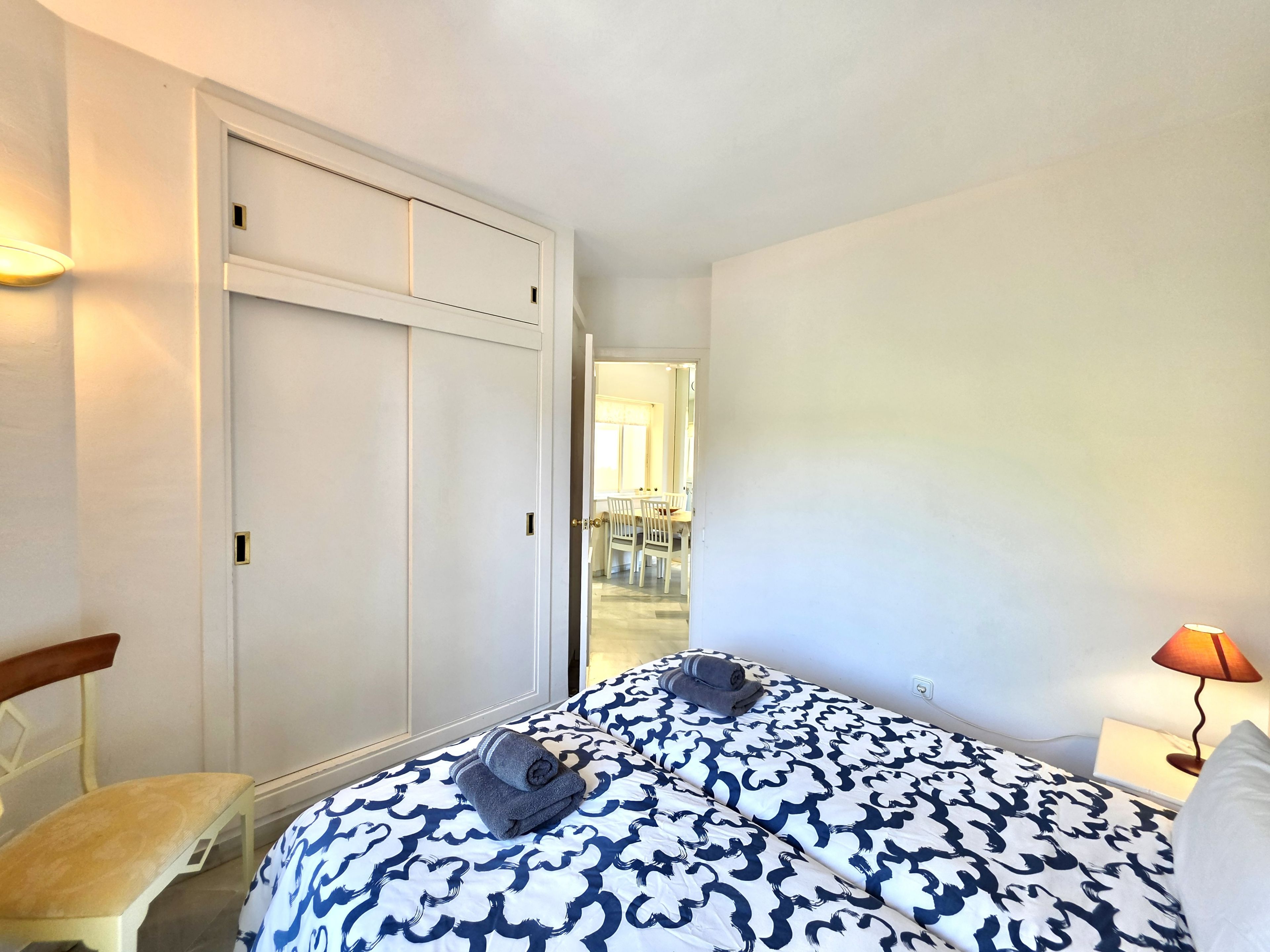 A hotel room with a bed, a chair, a lamp, and a wardrobe.