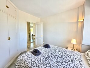 A hotel room with a bed, a nightstand with a lamp, a wardrobe, and a door leading to another room. - SR Cartuja 22, 2-Bedroom Apartment with Ocean View in Mijas Costa (Mijas)