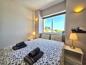 A hotel room with a bed, two bedside lamps, a window with a view, and a small table with a lamp. - SR Cartuja 22, 2-Bedroom Apartment with Ocean View in Mijas Costa (Mijas)