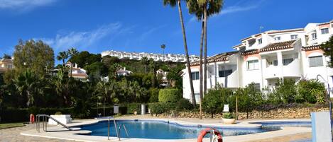 A swimming pool with a lifebuoy, palm trees, and a view of a hillside with buildings.