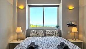 Ein Hotelzimmer mit einem großen Bett, zwei Nachttischlampen, einem Fenster mit Blick und einem kleinen Topfpflanzen auf der Fensterbank.