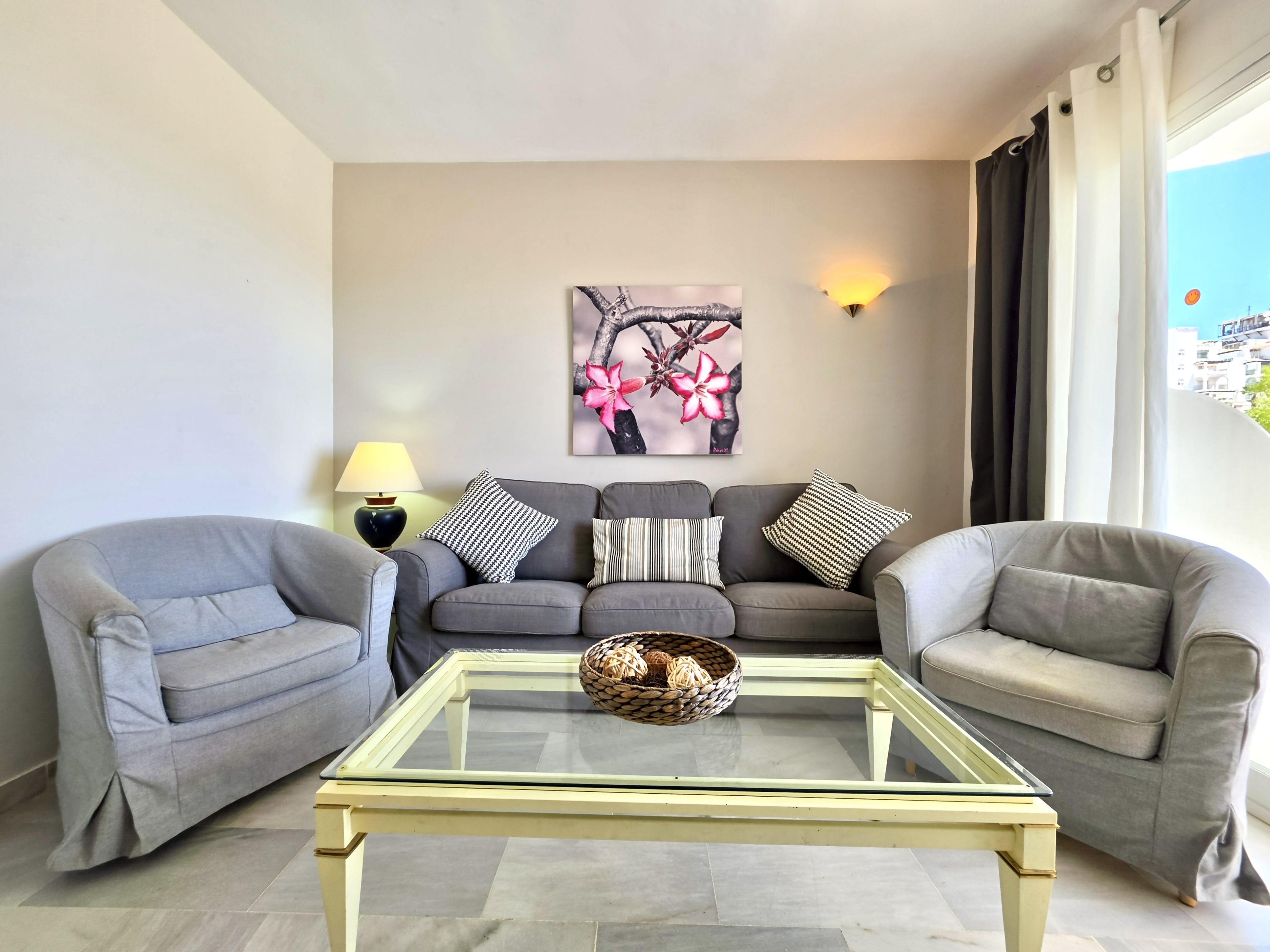 A living room with a sofa set, a glass coffee table, and a wall-mounted lamp.