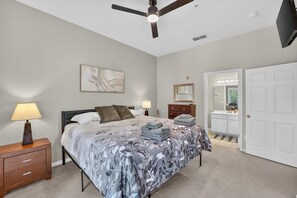 A bedroom with a bed, bedside tables, a ceiling fan, a door, and a bathroom with a mirror and sink. - 3BR/2BA Bahama Bay Pause in Davenport | Water View, Near Disney (Davenport)