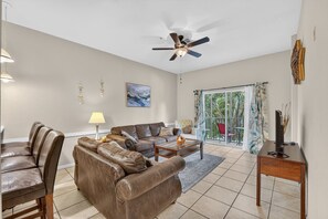 A spacious living room with a ceiling fan, a sofa set, a coffee table, and a television on a wooden stand. - 3BR/2BA Bahama Bay Pause in Davenport | Water View, Near Disney (Davenport)