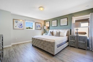 A bedroom with a large bed, a nightstand, a lamp, and artwork on the walls. - 6BR/4.5BA Kissimmee Home at Windsor at Westside, Pool (Kissimmee)